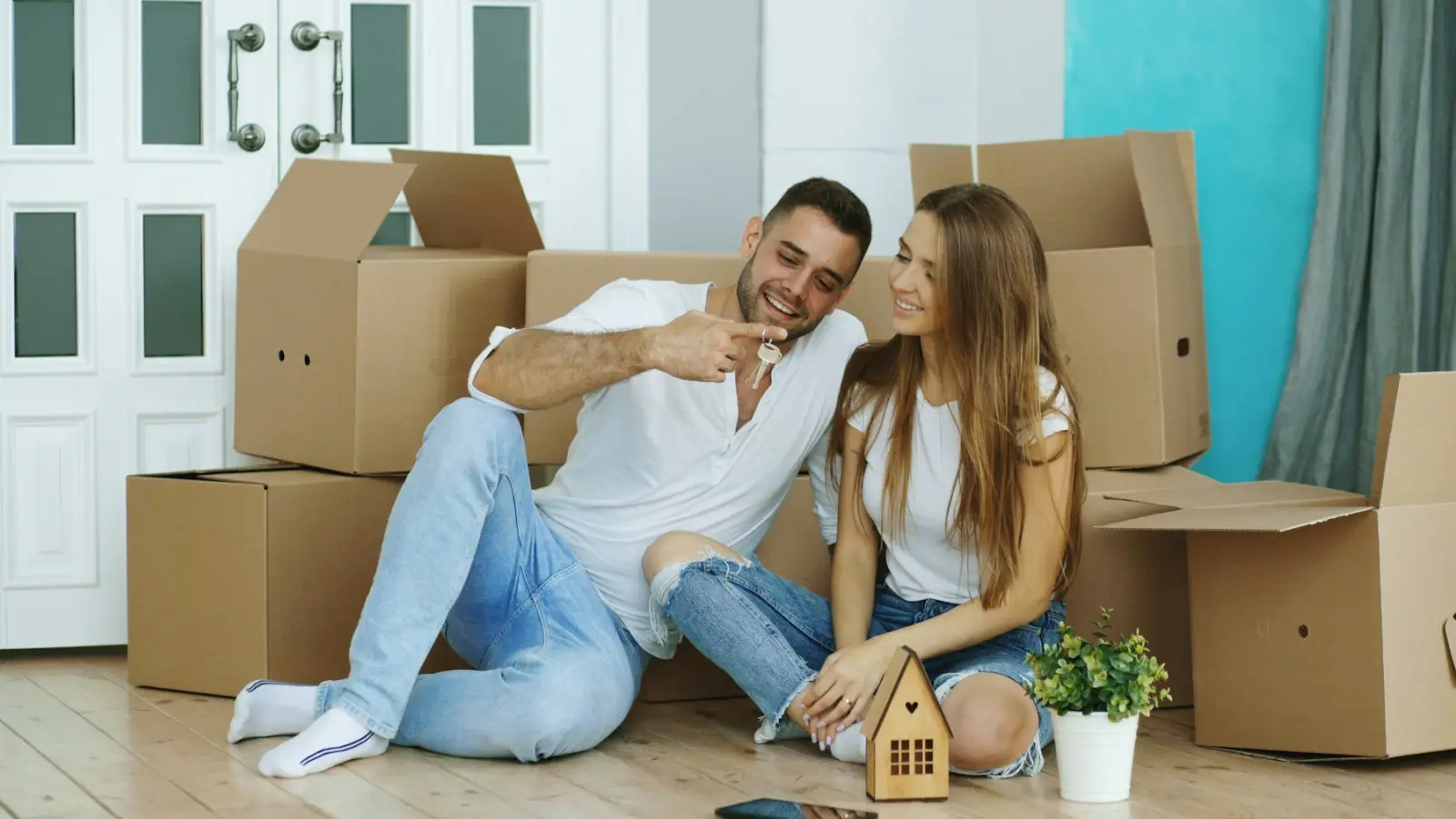 Paar zwischen Umzugskartons hält den Schlüssel zur neuen Wohnung
