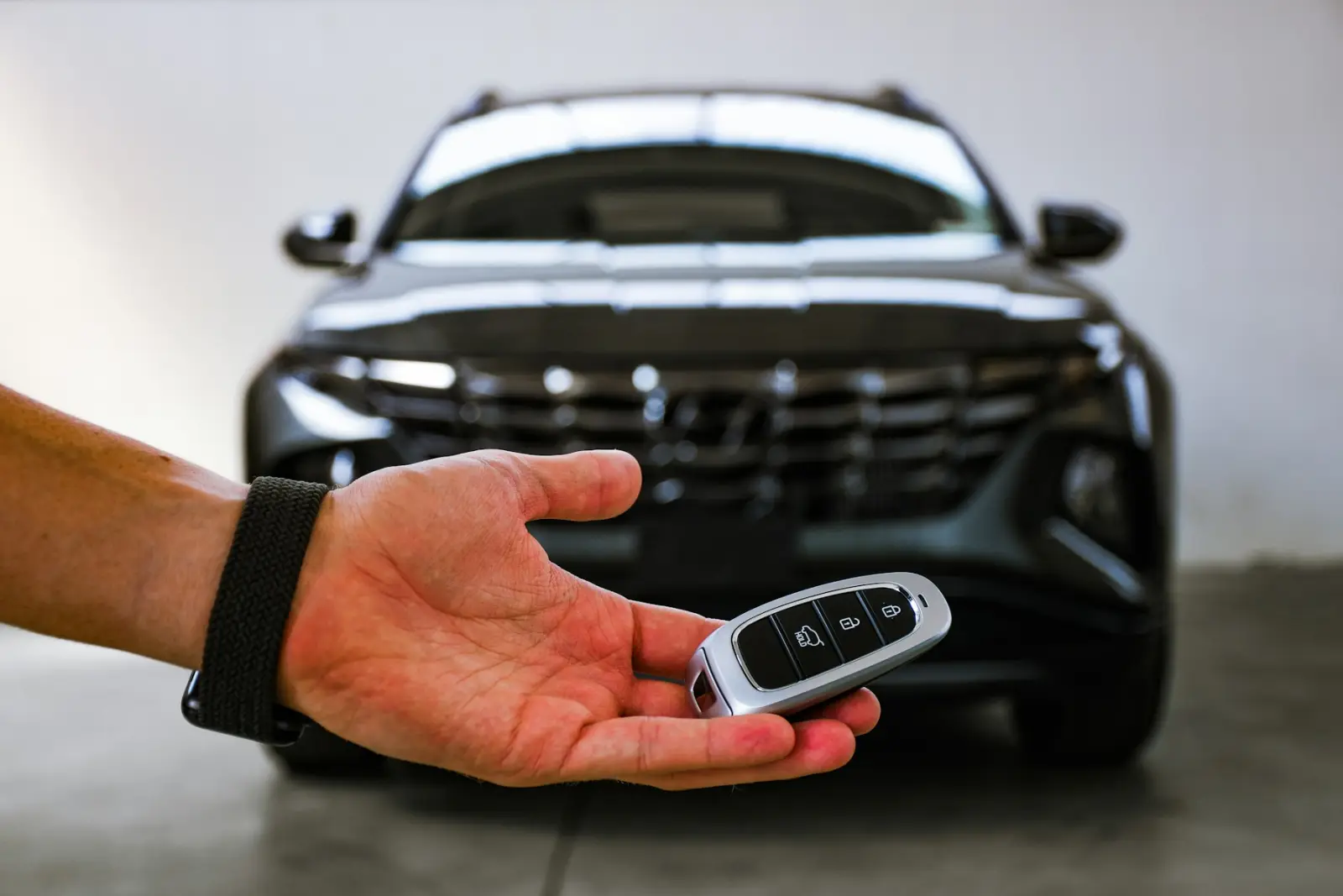 Hand mit Autoschlüssel vor einem neuen Fahrzeug